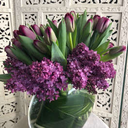 Purple tulips and lilac blooms arranged in a clear glass vase