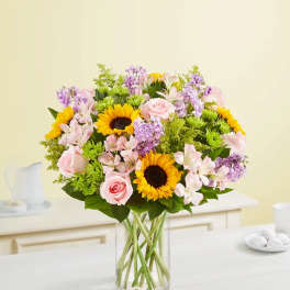 Mixed bouquet of sunflowers, pink roses, and lilac flowers in a glass vase