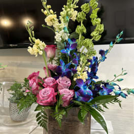 Pink roses and blue orchids in a wooden box with greenery