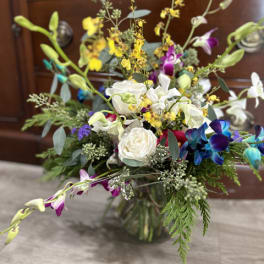 Mixed bouquet with white roses, orchids, and yellow accents in a glass vase