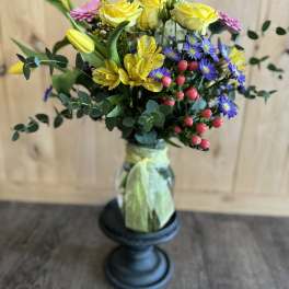 Bouquet of yellow roses, purple daisies, and pink blooms in a glass vase
