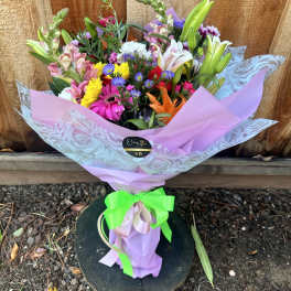 Mixed bouquet of colorful flowers wrapped in pink paper with a green ribbon