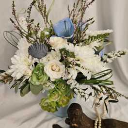 White and blue floral arrangement in a light blue vase with a shell accent
