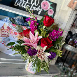 Bouquet of red roses, pink lilies, and purple flowers in a white mug vase
