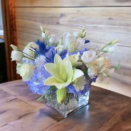 White lilies and blue hydrangeas in a square glass vase