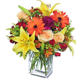 Mixed bouquet in a clear glass vase with lilies, roses, and orange daisies