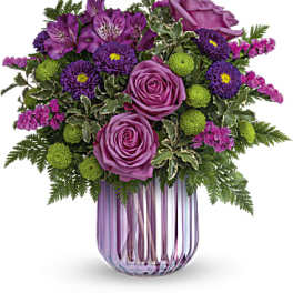 Purple roses and mixed purple flowers in a pink glass vase