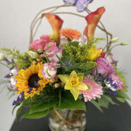 Mixed bouquet in a glass vase with sunflowers, pink blooms, and calla lilies