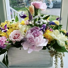 Mixed bouquet in a white rectangular vase with pink, yellow, white, and purple flowers