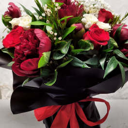 Bouquet of red and white flowers wrapped in black paper with a red ribbon