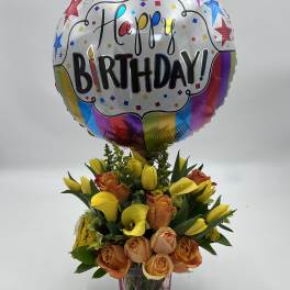 Birthday balloon above a bouquet of yellow calla lilies and peach roses in a vase