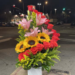 Bouquet of red roses, pink lilies, and sunflowers in a white vase