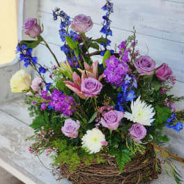 Mixed bouquet of lavender roses, lilies, and blue flowers in a twig basket
