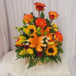 Mixed bouquet of orange roses, lilies, and sunflowers in a basket