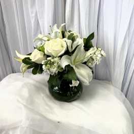 White roses and lilies arranged in a dark glass vase