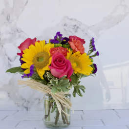 Bouquet of sunflowers, pink roses, and carnations in a glass vase