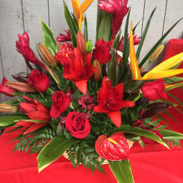 Red floral arrangement with orange tropical blooms and roses in a basket