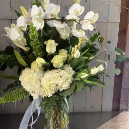 White orchids and pale flowers arranged in a clear glass vase with a ribbon.