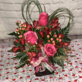 Pink roses and red alstroemeria in a black vase with a ribbon bow