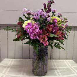 Mixed pink and purple flowers arranged in a glass jar vase