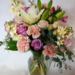 Pastel bouquet of lilies, roses, carnations, and mixed flowers arranged in a clear glass vase