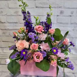 Pink and purple mixed flower arrangement in a pink box