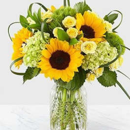 Sunflower bouquet with pale yellow roses in a clear glass vase