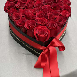 Heart-shaped box filled with red roses and a red satin ribbon