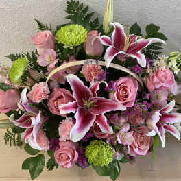 Pink roses and lilies arranged in a basket with green mums
