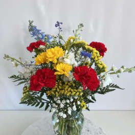 Mixed bouquet of red, yellow, white, and blue flowers in a glass vase