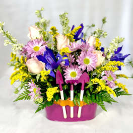Mixed bouquet in a pink container with small garden tools