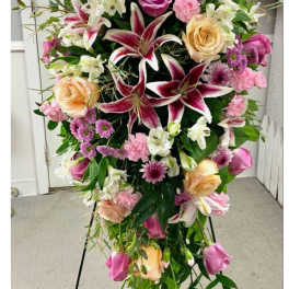 Standing floral spray with pink and peach roses and lilies on a black easel