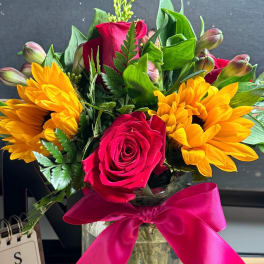 Bouquet of red roses and yellow flowers in a glass jar with a pink ribbon