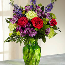 Bouquet of red roses, purple flowers, and green carnations in a green glass vase
