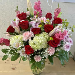 Mixed bouquet of red roses, pink flowers, and white lilies in a glass vase
