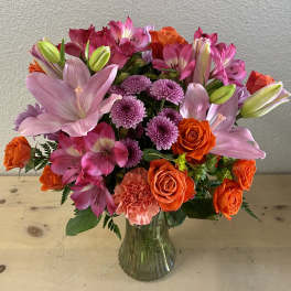 Bouquet of pink lilies, orange roses, and purple mums in a glass vase