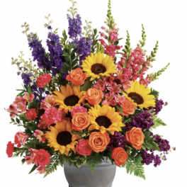 Mixed bouquet with sunflowers, orange roses, and purple spikes in a gray vase