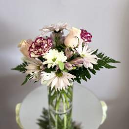 Mixed bouquet of pale daisies, carnations, and roses in a glass vase