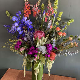 Tall mixed flower arrangement in a green vase with bright pink, blue, and orange blooms