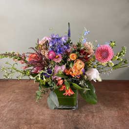 Mixed bouquet in a square glass vase with pink, purple, orange, and white flowers.