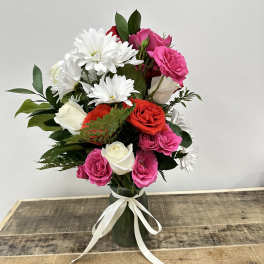Pink, red, and white roses with white daisies in a vase tied with ribbon.