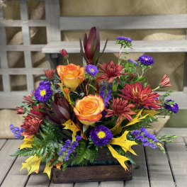 Autumn floral arrangement with orange roses and purple daisies in a wooden box