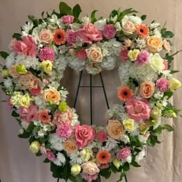 Heart-shaped floral wreath with pink, peach, and white flowers on an easel