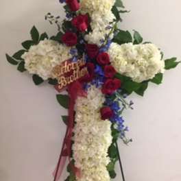 Cross-shaped floral tribute with white hydrangeas, red roses, and blue flowers