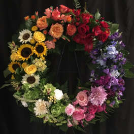 Colorful floral wreath with roses, sunflowers, and purple blooms on a black stand