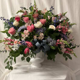 Large mixed flower arrangement in a white pedestal vase with a blue ribbon