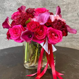 Pink and red roses with purple calla lilies in a clear glass vase