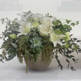 White lilies and roses in a round vase with trailing greenery