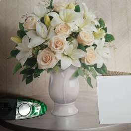 White lilies and pale roses arranged in a white vase