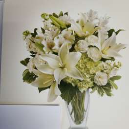White lilies and mixed white flowers in a clear glass vase